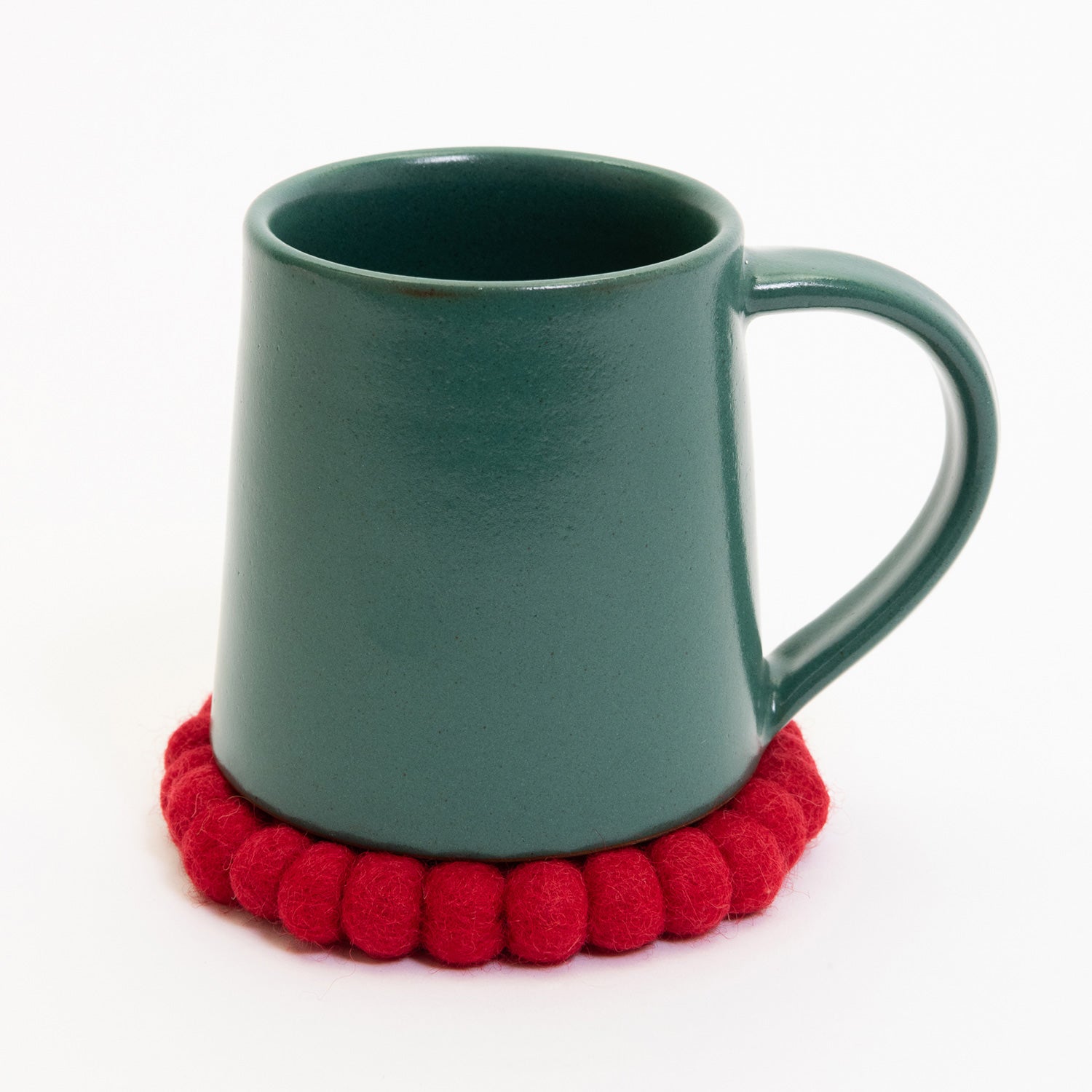 A teal coloured stoneware mug pictured on a white background. The mug is sitting on a red felt coaster.
