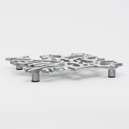 A side view of the stainless steel silver seaweed shaped trivet with black pads on the feet.