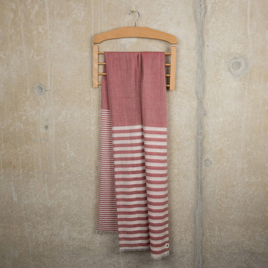 A photo of the scarlet strip scarf hanging on a rustic concrete background. The scarf has red and white stripes.